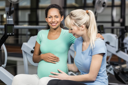 微笑的女人坐着触摸孕妇的肚子
