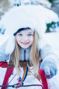 在美丽的雪天玩雪橇的可爱女孩