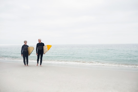 带冲浪板的老年夫妇在海滩上散步
