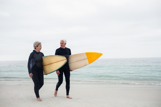 带冲浪板的老年夫妇在海滩上散步