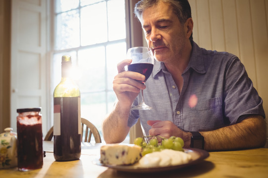 成熟的男人坐在桌旁品尝红酒