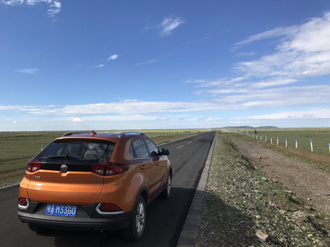 蓝天白云下草原公路上的橙色汽车