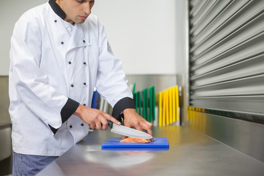厨师在蓝色砧板上用刀切生鲑鱼