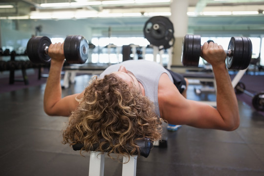 年轻肌肉男在健身房用哑铃锻炼