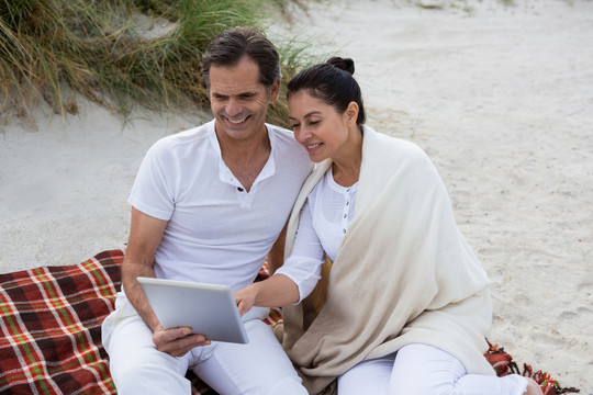 在海滩上使用平板电脑的快乐夫妻