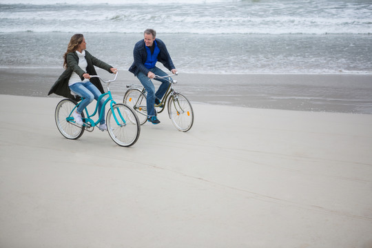 冬天在海滩上骑自行车的夫妇