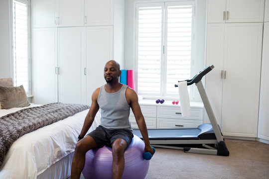 男子在家卧室用哑铃练习健身球