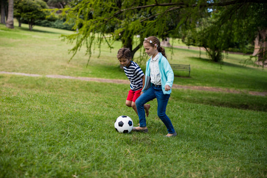 在公园踢足球的男孩和女孩