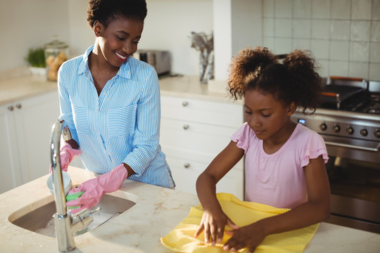 母亲帮助女儿在家里洗餐具