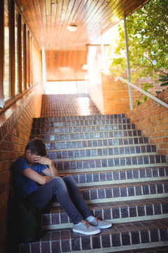 小男孩独自坐在学校的楼梯上