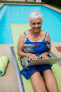 在泳池边的躺椅上休闲的老年妇女