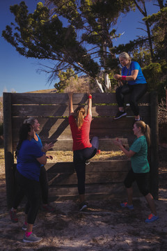 女子在队友的鼓励下爬上一堵木墙
