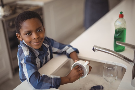 厨房水槽里洗杯子的微笑男孩