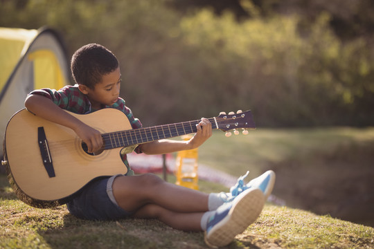 在公园里弹吉他的微笑男孩