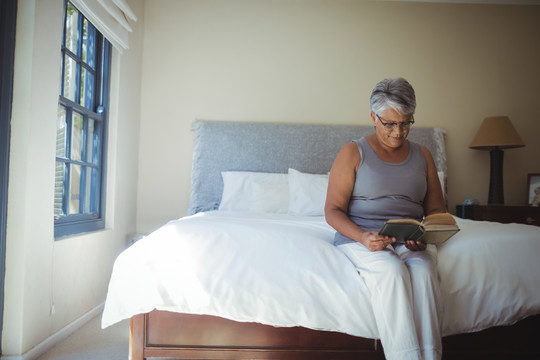 老年妇女坐在卧室的床上看书