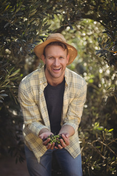 一个年轻人站在农场树旁拿着橄榄