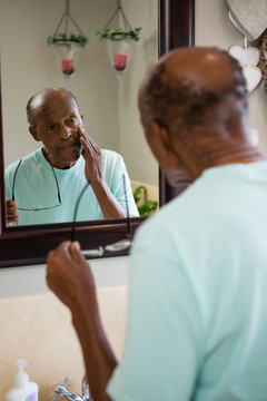 老人一边看镜子一边摸脸颊