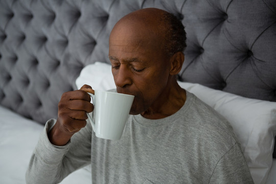 老人坐在床上喝咖啡