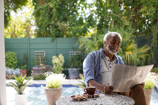 老人坐在院子里的桌子边看报纸