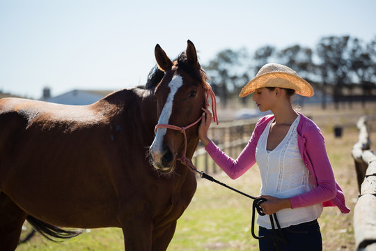 年轻女子牵着马站在牧场上