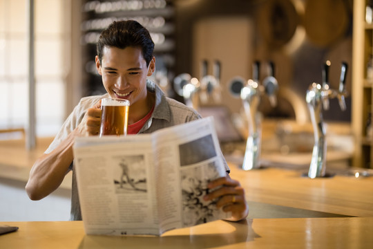 在餐馆看报纸时喝啤酒的男人