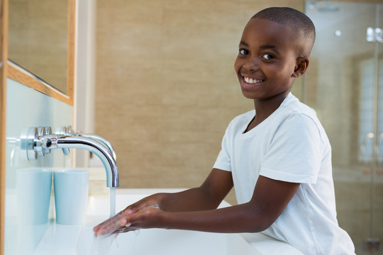 在浴室洗手池洗手的微笑男孩