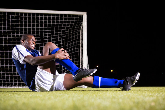 男性足球运动员坐操场上膝盖疼痛