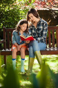 母亲坐在木凳上给女儿看书