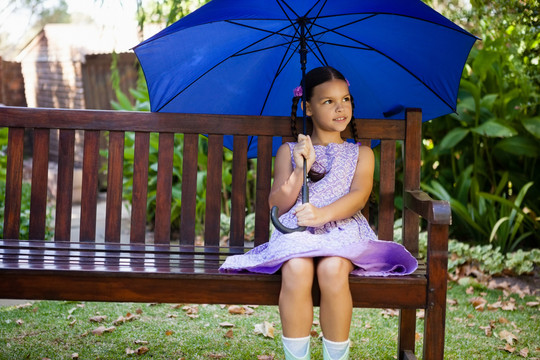 坐在木长椅上带着蓝色雨伞的女孩