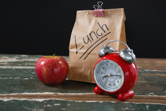 闹钟和木制桌上的午餐袋