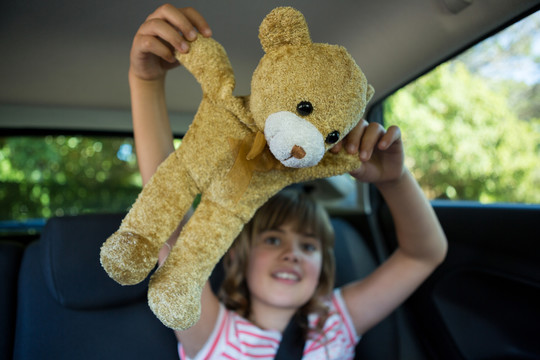 在汽车后座上玩泰迪熊的少女