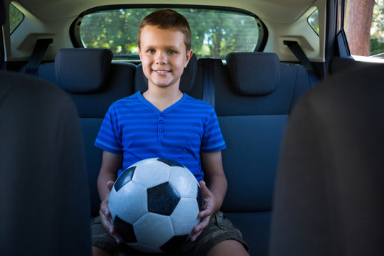 快乐的少年坐在汽车后座上踢足球