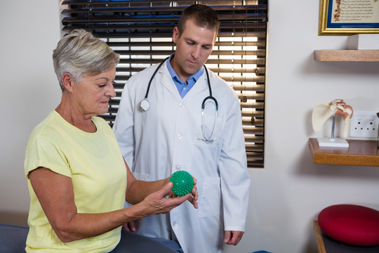 理疗师协助老年妇女做压力球运动