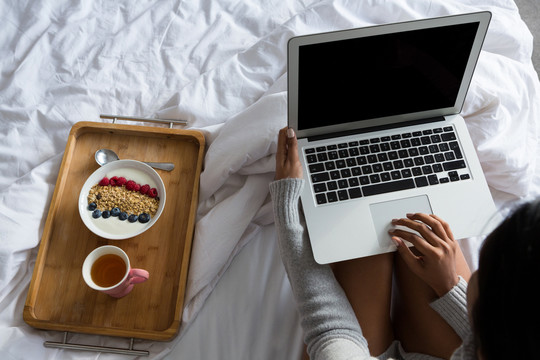 带笔记本电脑的女人在床上吃早餐