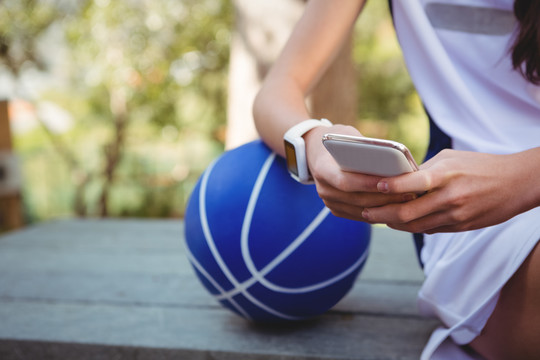 女性在倚靠篮球时用智能手机