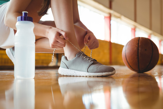 篮球场女子蹲地系鞋带特写镜头