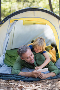 快乐的父子在营地帐篷里玩手机
