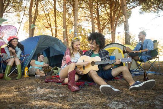 年轻女子和男朋友在野营地弹吉他