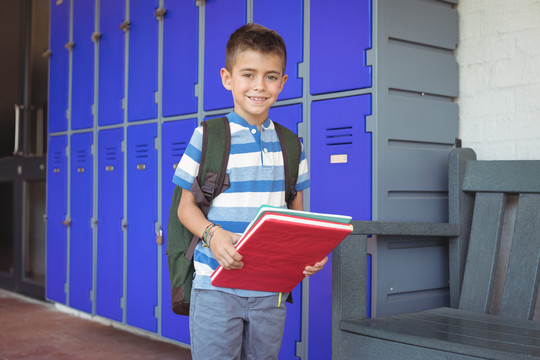 学校走廊里拿书的微笑男孩