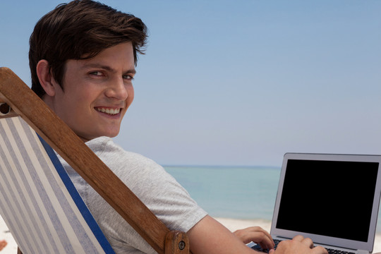 男人坐在沙滩上用笔记本电脑