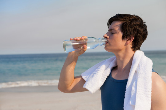 男人在沙滩上喝着瓶子里的水