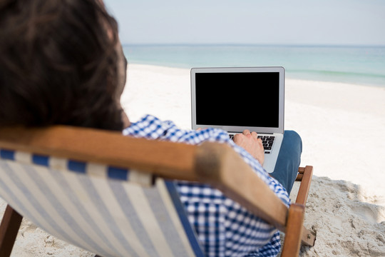 坐在沙滩躺椅上用笔记本电脑的人