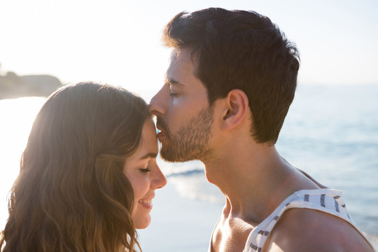 年轻男子在海滩亲吻女友额头