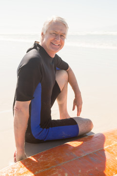 沙滩上坐在冲浪板旁微笑的老人