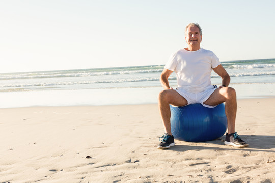沙滩上坐在球上微笑的老人