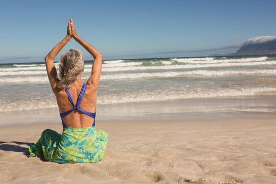 坐在沙滩上练习瑜伽的老妇人