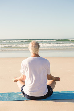 坐在沙滩上练瑜伽的老人