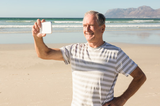 在沙滩上用手机拍照的老人