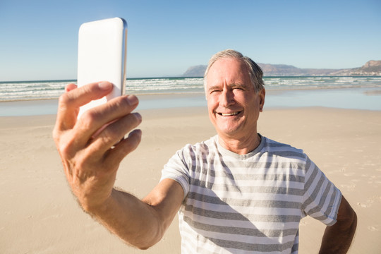在沙滩上用手机拍照的老人
