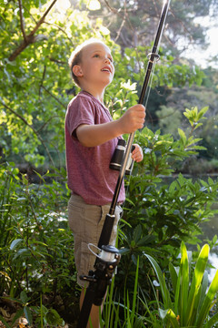 男孩看着森林里河边的鱼竿